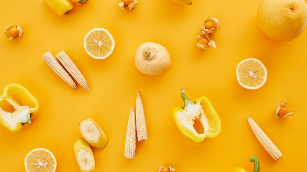 An artistic flat lay of assorted yellow fruits and vegetables against a yellow surface, showcasing a healthy lifestyle.